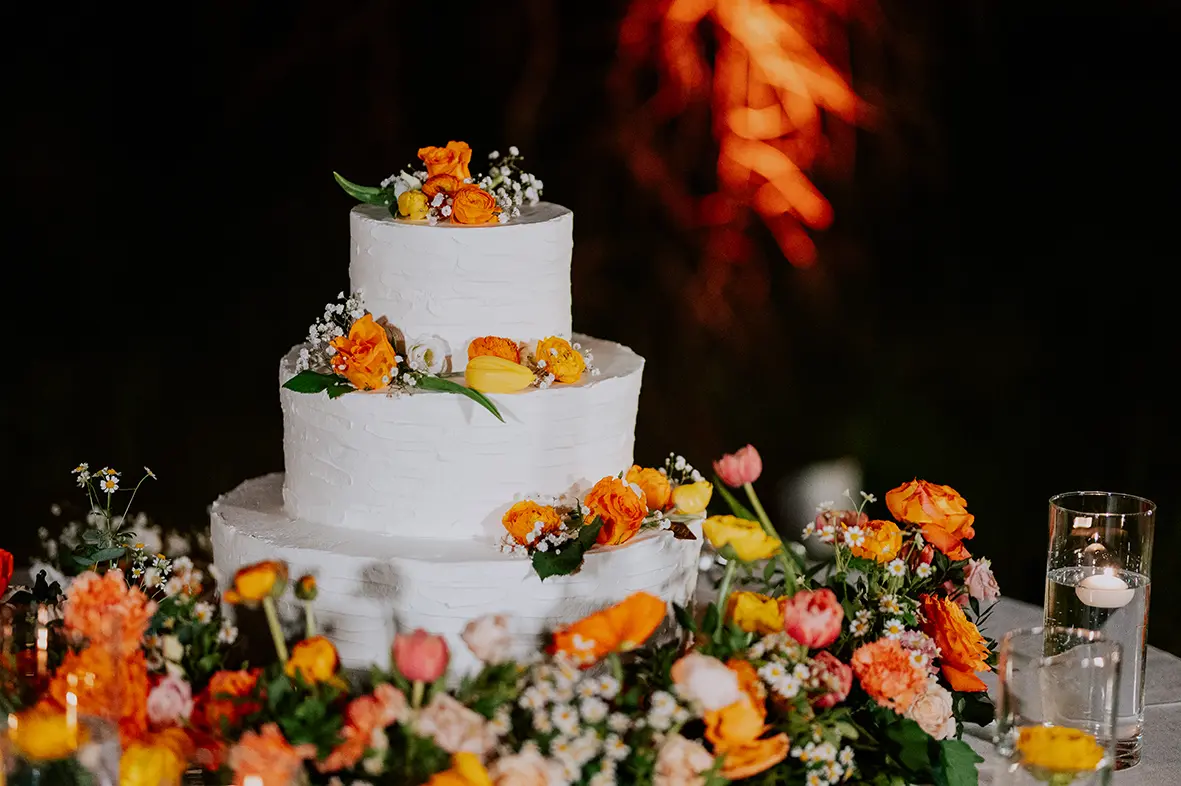 Una torta nuziale adagiata su un tavolo imbandito di fiori e decorata con gli stessi.