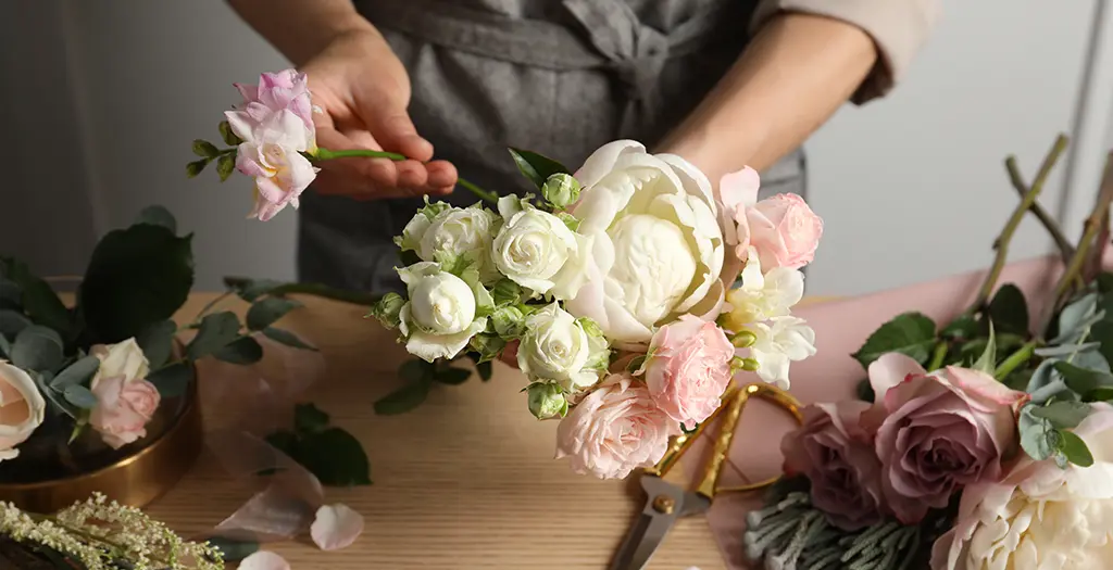 Una fiorista mentre prepara un bouquet con rose bianche e rosse e peonie.